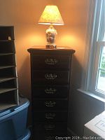 Tall chest of drawers showing five drawers with ornate metal handles in a dark wood finish