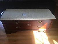 Full front view of Lane cedar chest showing brass hardware, carved center medallion, and cream upholstered top with heart texture.