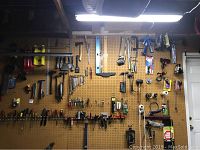 Wide view of pegboard wall with various hand tools including hammers, wrenches, pliers, clamps, measuring tapes, and saws.