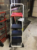 Front view of the Cosco step ladder showing four steps with black plastic treads and red top platform, white metal frame.