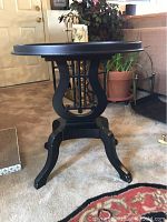 Front view of black harp style side table, showing round top and harp-shaped central support with curved legs.