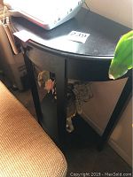 Black half moon wooden table against wall beside couch, showing curved top and bottom shelf, slight wear visible