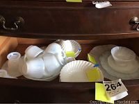 Multiple opalescent glass dishware pieces including bowls, plates, and small cups. White translucent glass. Several pieces stacked and grouped showing wear and chipping.