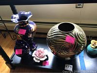Photo showing four items: blue and white ginger jar, brass vase with swirl pattern, pink and white ceramic rose, small blue flower pot with brass flower.