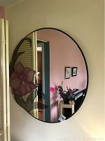 Full view of round mirror showing pink flower applique on the left side, black frame and reflective surface.