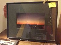 Frontal view of the larger framed photograph showing a nighttime landscape with lights and dim sunset.