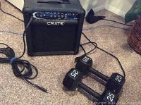 Photo showing Crate XT 15R guitar amplifier and two 25-pound hex dumbbells on carpeted floor with amplifier plugged in via cable.