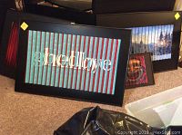 Black-framed optical art prints arranged on carpet with largest 24x36 inch "goodbye" print in front.