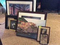 Photo showing a collection of framed art and prints leaning against a wall with a variety of sizes and styles including canvas art and posters