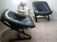 Two black leather chairs shown side by side in corner of room