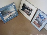 Three framed photographs leaning against wall on the floor showing the overall lot contents.