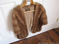 Brown fur jacket hanging on wooden hanger with visible interior lining showing cracks and tears.