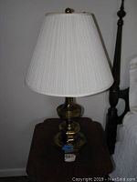 Full view of the ceramic table lamp with fabric crepe shade on a wooden side table next to a bedpost.