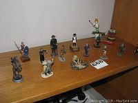 Photo showing a collection of fourteen hand painted lead figurines, some mounted, arranged on a wooden surface.
