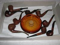 Eight briar pipes arranged around amber glass ashtray in tray