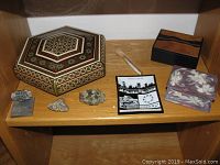 Shelf with hexagonal cloisonne wood box, iron pyrite specimens, Montreal Expo ashtray, small wooden and purple floral boxes, and Porsche engine sculpture