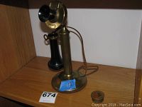 Full view of candlestick phone standing on wooden shelf beside metal pillbox