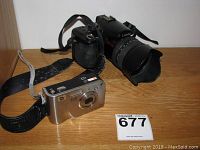 Photo of two cameras: Lumix DMC-FZ50 DSLR-style black camera with large lens and strap, and HP Photosmart R707 compact silver digital camera on wooden surface.