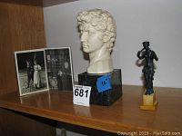 Two sculptures on wooden shelf with 5x7 photographs behind them.