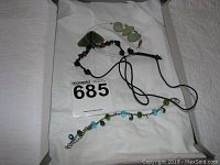 Bracelet with blue and green beads, green bead necklace, and black cord necklace laid out together