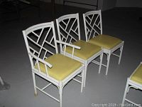 Photo of six Meadowcraft metal dining chairs arranged side by side with two armchairs and four armless chairs, white bamboo-style frames and yellow vinyl cushions.