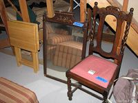 Photo showing hand carved dark wood dining chair with dusty rose upholstered seat next to matching framed mirror and folding cocktail tables visible in the background.