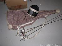 Fencing foils laid out next to the fencing mask and padded carrying case on a gray floor.
