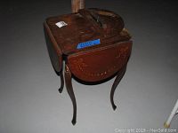 Show top view of wooden drop leaf table with one leaf detached and lying on top, visible wear and scratch marks.