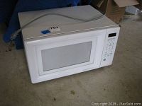 White General Electric microwave oven resting on concrete floor. Shows front view with door window and control panel.