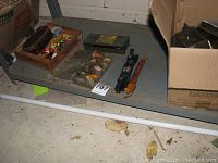 View of whole lot as placed on a shelf including fishing lures in wooden tray, fillet knife, light fixture, and hardware box