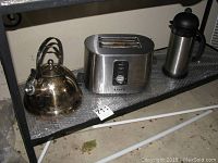 Overview of the three items on a shelf: Krups toaster, metal tea kettle, and stainless steel coffee thermos.