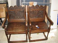 Front view of two carved oak chairs side by side showing carved back panels and armrests