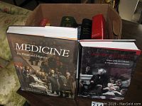 Photo showing 'Medicine: An Illustrated History' and 'Adorn the Halls' books on top of a box of other books.
