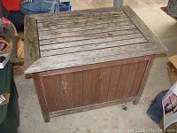 View of the teakwood ice cooler chest showing worn and weathered slatted wood top and reddish brown side panels.