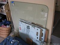 Clear glass square tabletop leaning against a wall with cardboard boxes and packing materials around.