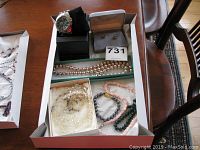 Overview of lot showing men's wristwatch on black cushion, three beaded necklaces, small pairs of earrings, and a boxed white pearl-like beaded necklace.
