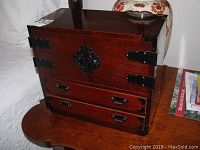 Front and side view of the rectangular wooden jewelry box showing black metal hinges, corner brackets and handles on the front double doors and drawers.