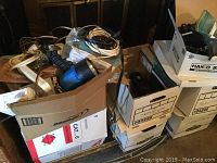 View showing several cardboard boxes labeled with contents, filled with various wires, tools, and accessories including visible blue flashlight and lamp.