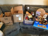 Photo of three cardboard boxes and plastic containers holding the full lot including dolls, toys, music boxes, lamp, and games.