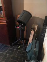 Black telescope stand with gray cylindrical mount on floor