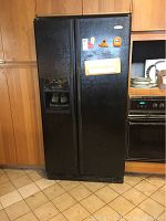 Exterior view of the black Whirlpool side-by-side refrigerator installed in kitchen cabinetry.