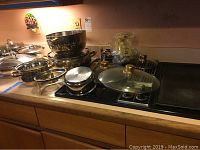 Wide angle photo of nested Command Performance Gold stainless steel cookware pans and chafing dishes with glass lids on countertop.