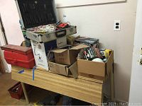 Overview of folding table with open cases and cardboard boxes containing test meters, cables, bulbs and ties