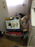 Photo showing Wagner Power Roller paint sprayer box on top of plastic container with painting supplies and shopping bag with more supplies.