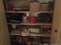 Shelving unit containing folded towels, white plastic containers, boxes, a humidifier, clothes steamer, and miscellaneous household items.