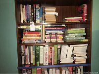 Full view of bookshelf containing assorted cookbooks, gardening guides, home repair manuals, and novels in hardcover and paperback.