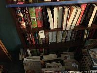 Wide view of wooden shelves containing multiple cooking books arranged side by side, including visible titles such as The Cook Book and others.