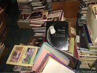 Overview of books including New Atlas of the Moon on top of a stack, surrounded by other books and craft papers