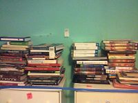 Three stacks of assorted books on top of a cabinet against a teal wall