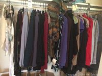 Full view of assorted women’s clothing hanging on rack showing multiple jackets, blazers, and dresses in various colors including red, beige, purple, black, and patterned woven fabrics.